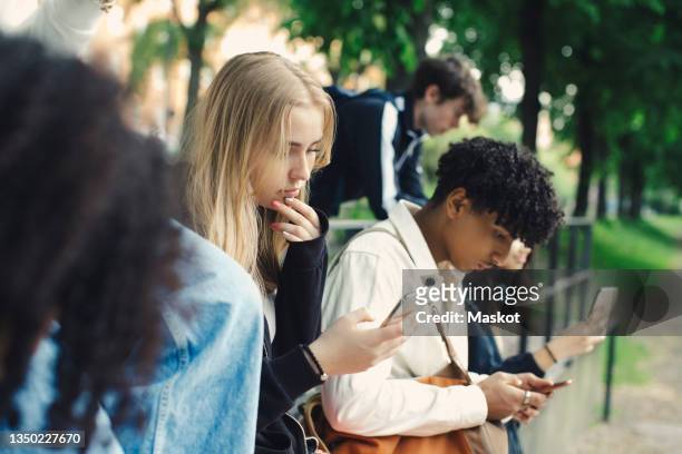 male and female friends using smart phones in park - social media stock pictures, royalty-free photos & images