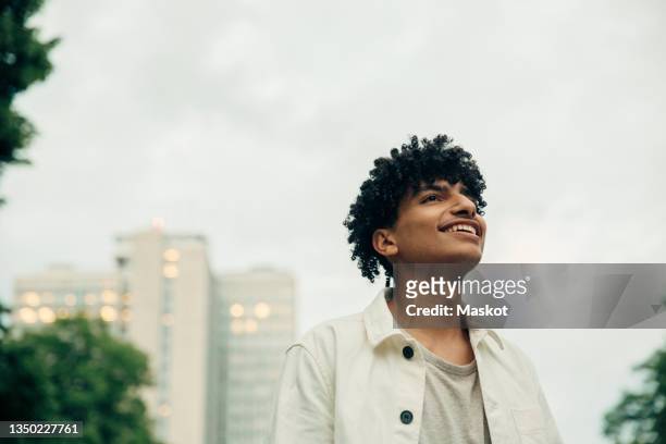 smiling teenager boy contemplating against sky - boy thoughtful stock-fotos und bilder
