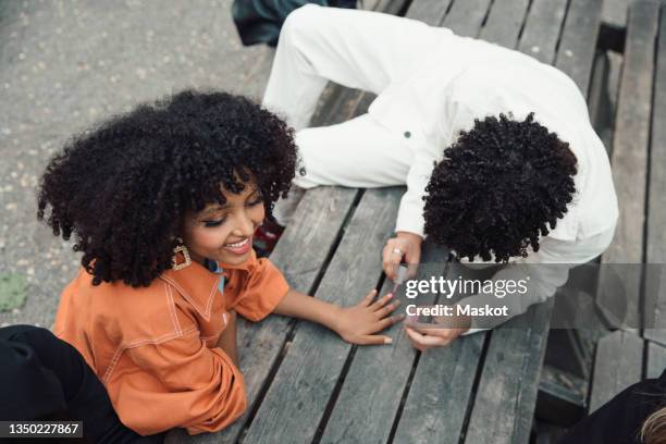 high angle view of male teenager applying nail polish to female friend while sitting on table - lackierte-fingernägel-finger stock-fotos und bilder