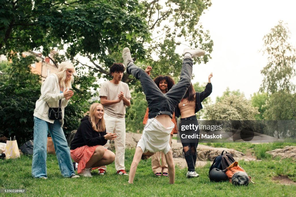 Multiracial friends cheering teenage boy doing handstand at park