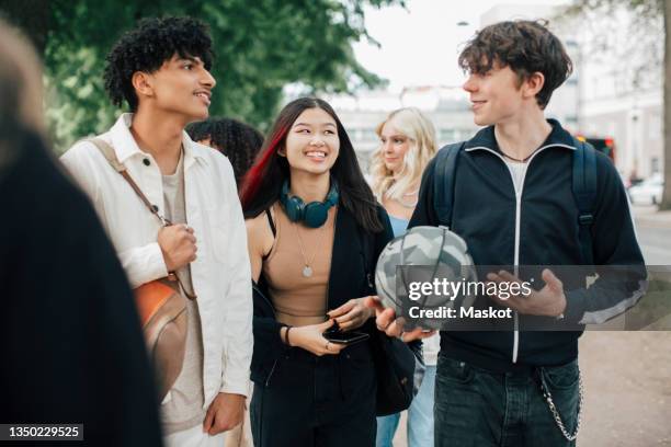 smiling male and female friends talking while walking in park - ティ�ーンエイジャーのみ ストックフォトと画像