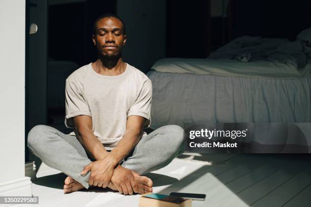 mid adult man meditating with eyes closed in sunlight at home - zen stock-fotos und bilder