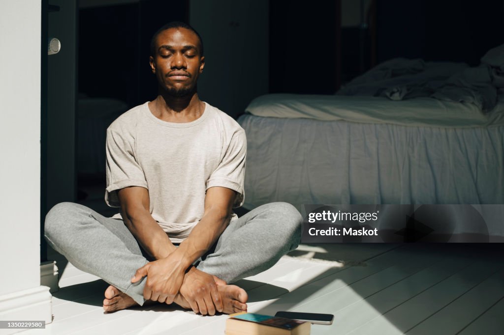 Mid adult man meditating with eyes closed in sunlight at home