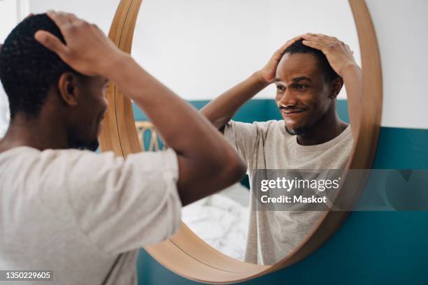 smiling man with hand in hair looking in mirror at home - hand in hair imagens e fotografias de stock