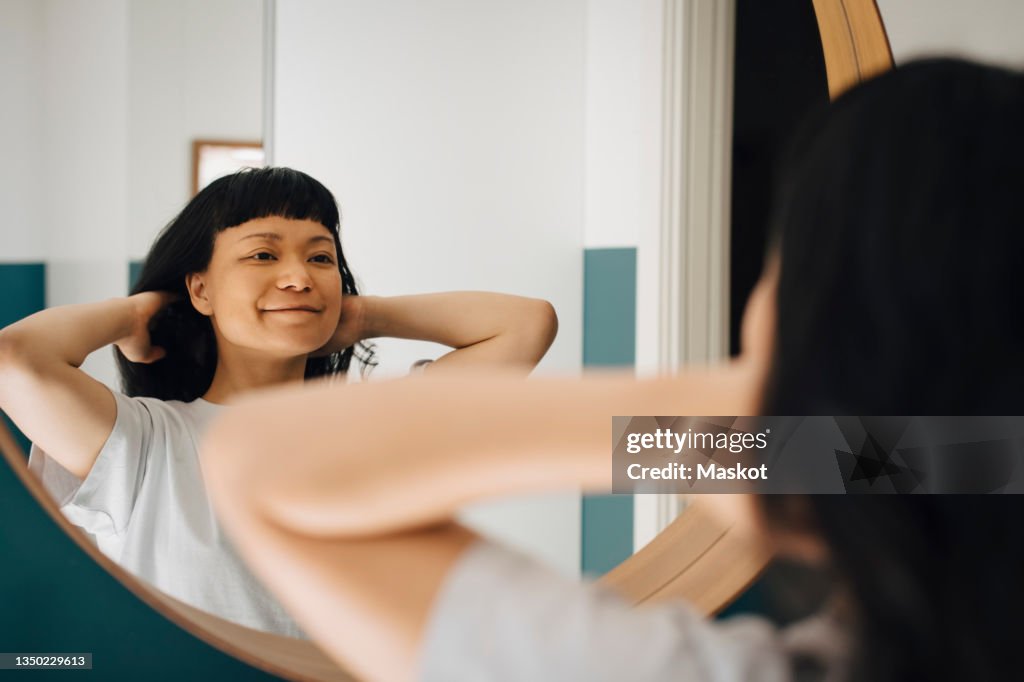 Reflection of smiling woman with hand in hair at home