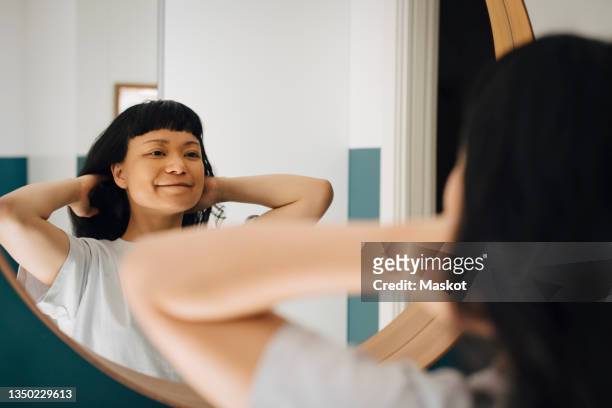 reflection of smiling woman with hand in hair at home - mirror stockfoto's en -beelden