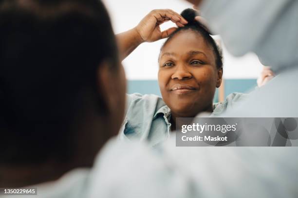 smiling woman adjusting hair while looking in mirror at home - 髪に手をやる　女性 ストックフォトと画像