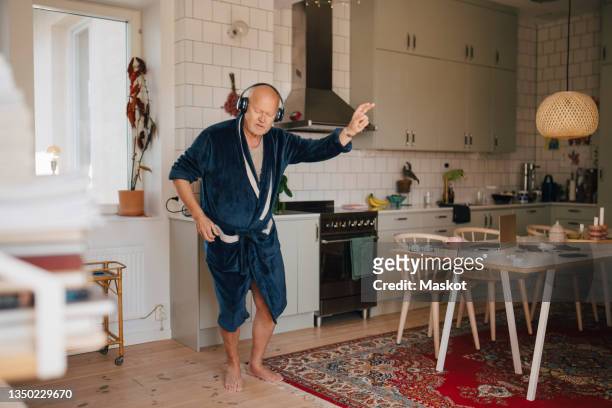 senior man dancing while enjoying music through headphones in kitchen - senior heureux photos et images de collection