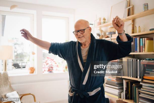 senior man in bathrobe dancing in living room at home - elderly dancing stock-fotos und bilder