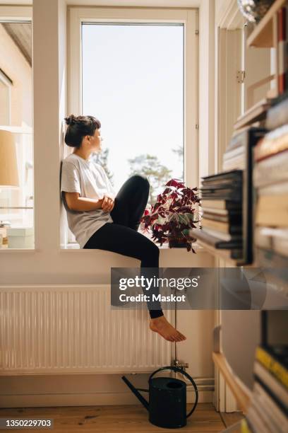 young woman sitting in window at home - peitoril de janela - fotografias e filmes do acervo