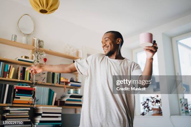 happy mid adult man dancing with coffee cup in living room at home - coffee happy stockfoto's en -beelden