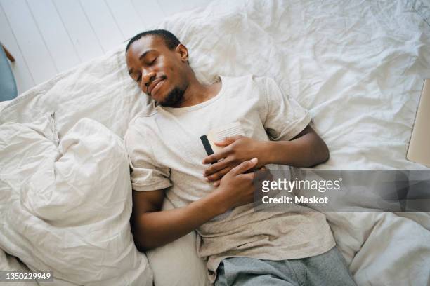 mid adult man sleeping with book on bed in bedroom - black man sleeping in bed stock pictures, royalty-free photos & images