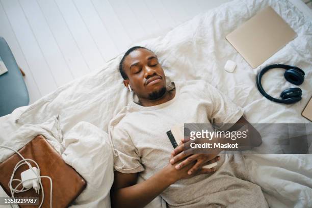 Directly above view of man sleeping with book on bed at home