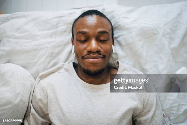 smiling man wearing wireless in-ear headphones while relaxing with eyes closed - man relaxing stockfoto's en -beelden