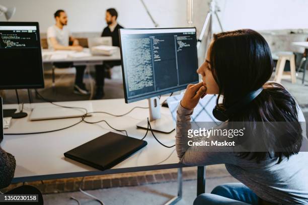 female hacker looking at computer while working in startup company - coder stock-fotos und bilder