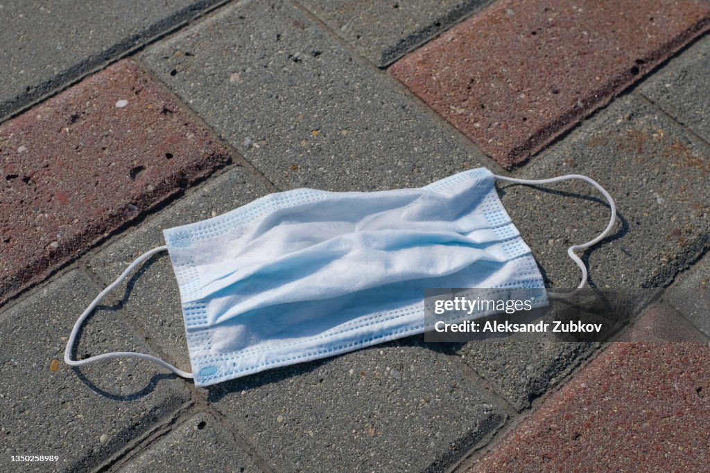 Used lost protective medical face mask on the ground. A disposable mask is lying on the sidewalk outside. Improper disposal of garbage, littering of the planet, a worldwide environmental problem in connection with the coronavirus and the wrong way of life
