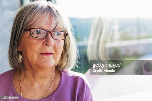 pensive mature woman looking out of the window - 60 69 years stock pictures, royalty-free photos & images