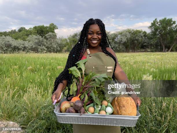 portrait of a happy young african american woman standing at the door of a walk-in refrigerator holding a basket of delicious, healthy, organic produce at a local small business farm-to-table supplier in colorado - afro caribbean and american stock pictures, royalty-free photos & images