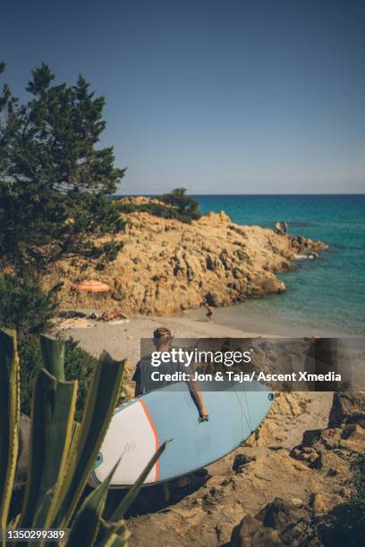 young man carrying paddle board walks down to sea - escapisme stockfoto's en -beelden