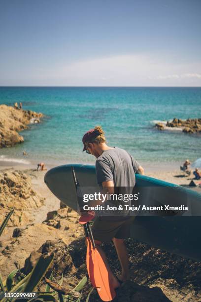 young man carrying paddle board walks down to sea - paddle board men imagens e fotografias de stock