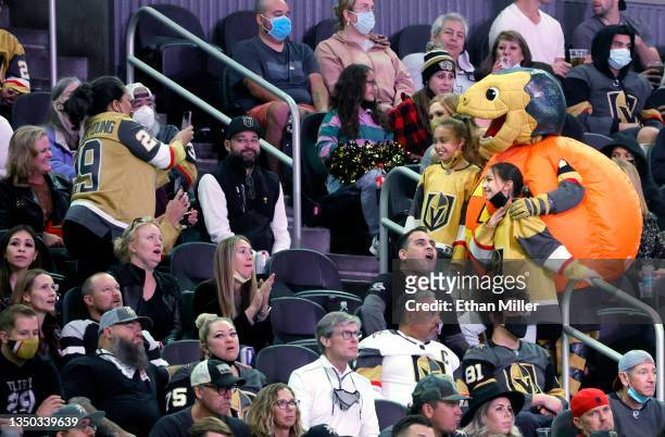 The Vegas Golden Knights mascot Chance the Golden Gila Monster, wearing a jack-o'-lantern costume, poses with fans in the stands in the third period...
