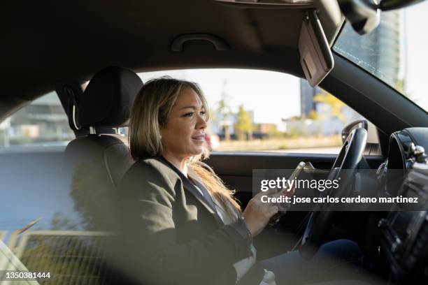 mature business woman in car interior looking at her mobile phone - business person driving stock-fotos und bilder