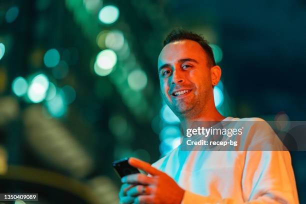 handsome man using smart phone in city at night - neon lighting smiling stock pictures, royalty-free photos & images