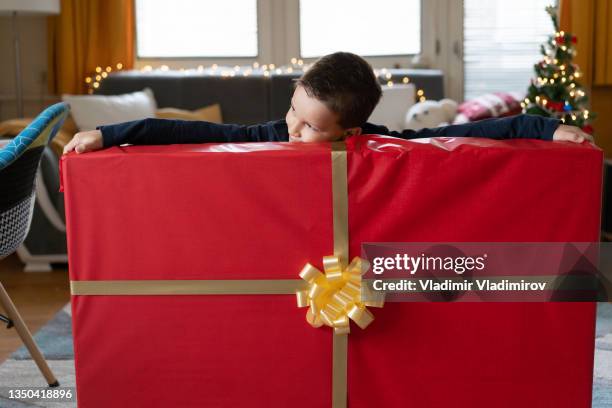 a small boy trying to reach both ends of a very large christmas present - big xmas stocking stock pictures, royalty-free photos & images