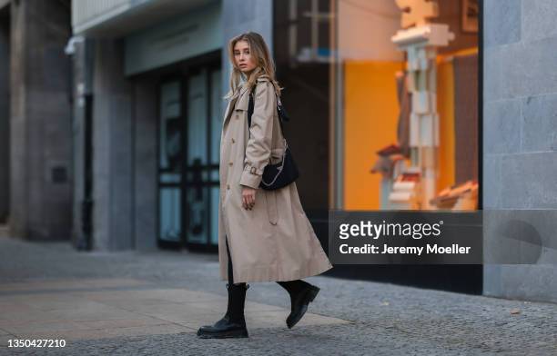 Lisa Mottl wearing a beige trench coat, a moschino belt, a black prada bag, black pants and Copenhagen Studios black boots on October 29, 2021 in...