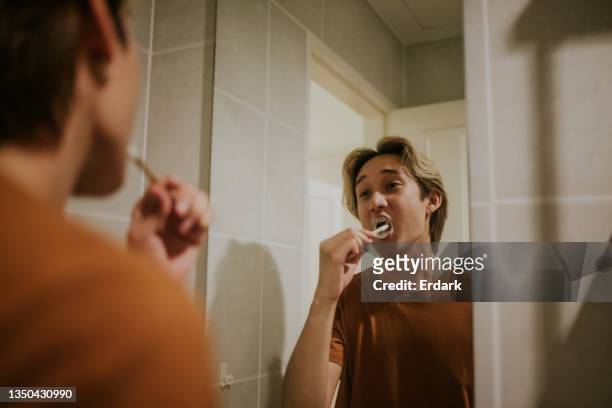junger schwuler mann errötet zähne mit nachhaltiger zahnpasta und holzzahnbürste auf dem spiegelstockfoto - zähne putzen stock-fotos und bilder