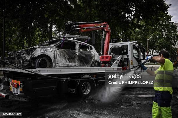 Worker cleans the street next to a burnt car loaded onto a towing truck in the Aubiers neighborhood in Bordeaux, south-western France on late June 30...