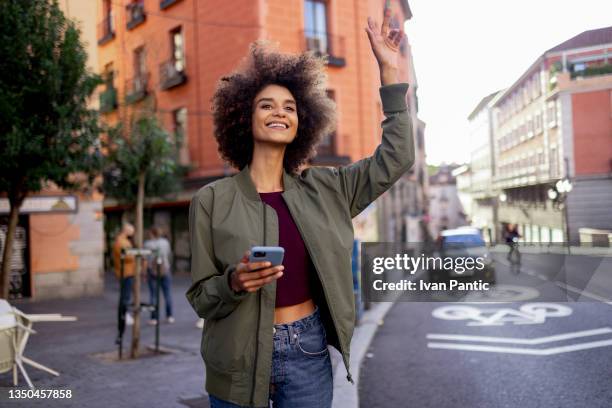 happy young mixed race woman using a smart phone to call for an uber - uber taxi app in madrid stock pictures, royalty-free photos & images