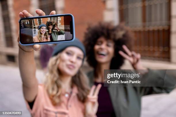 duas jovens amigas tirando fotos com um telefone inteligente - pose alternativa - fotografias e filmes do acervo