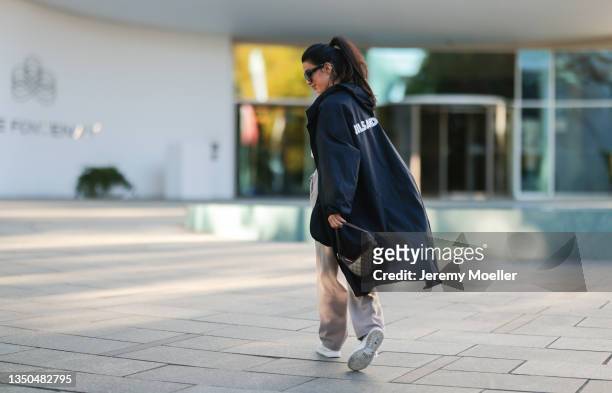 Semra Hunt wearing Nike Air Force white sneaker, beige jogging pants, a Jil Sander black parka, a white shirt, Celine black shades and Gucci mini...
