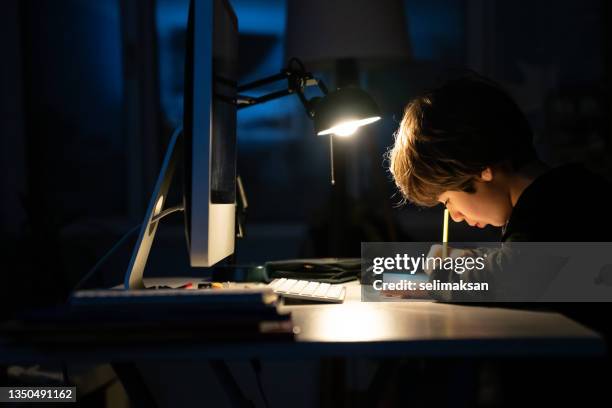 photo of elementary schoolboy studying at home in dark - bureaulamp stockfoto's en -beelden