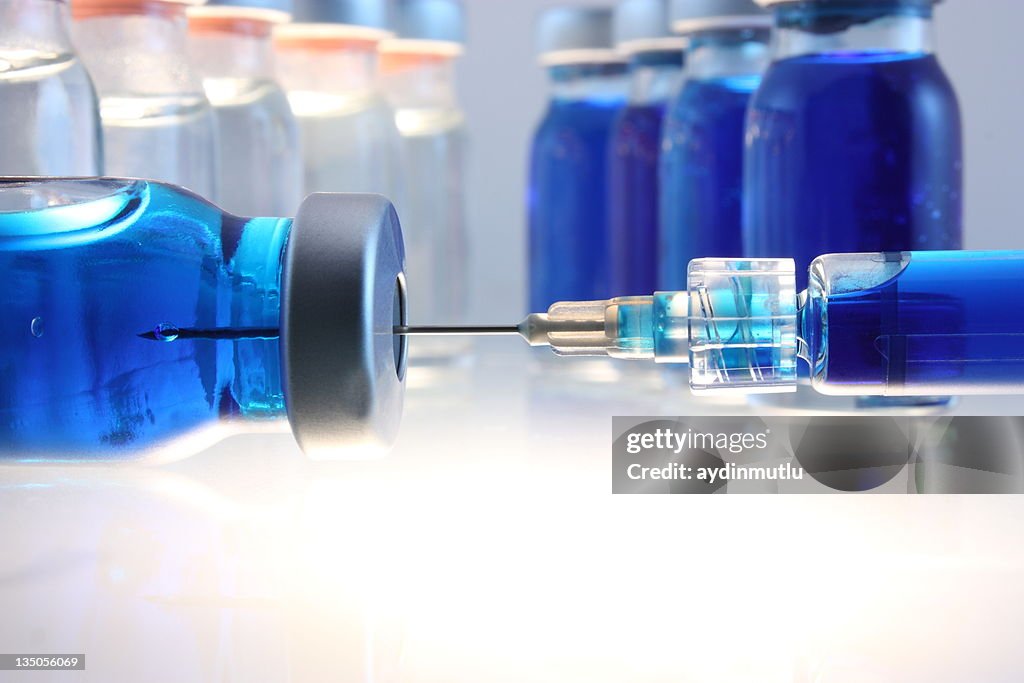 Syringe with blue liquid entering bottle with more behind