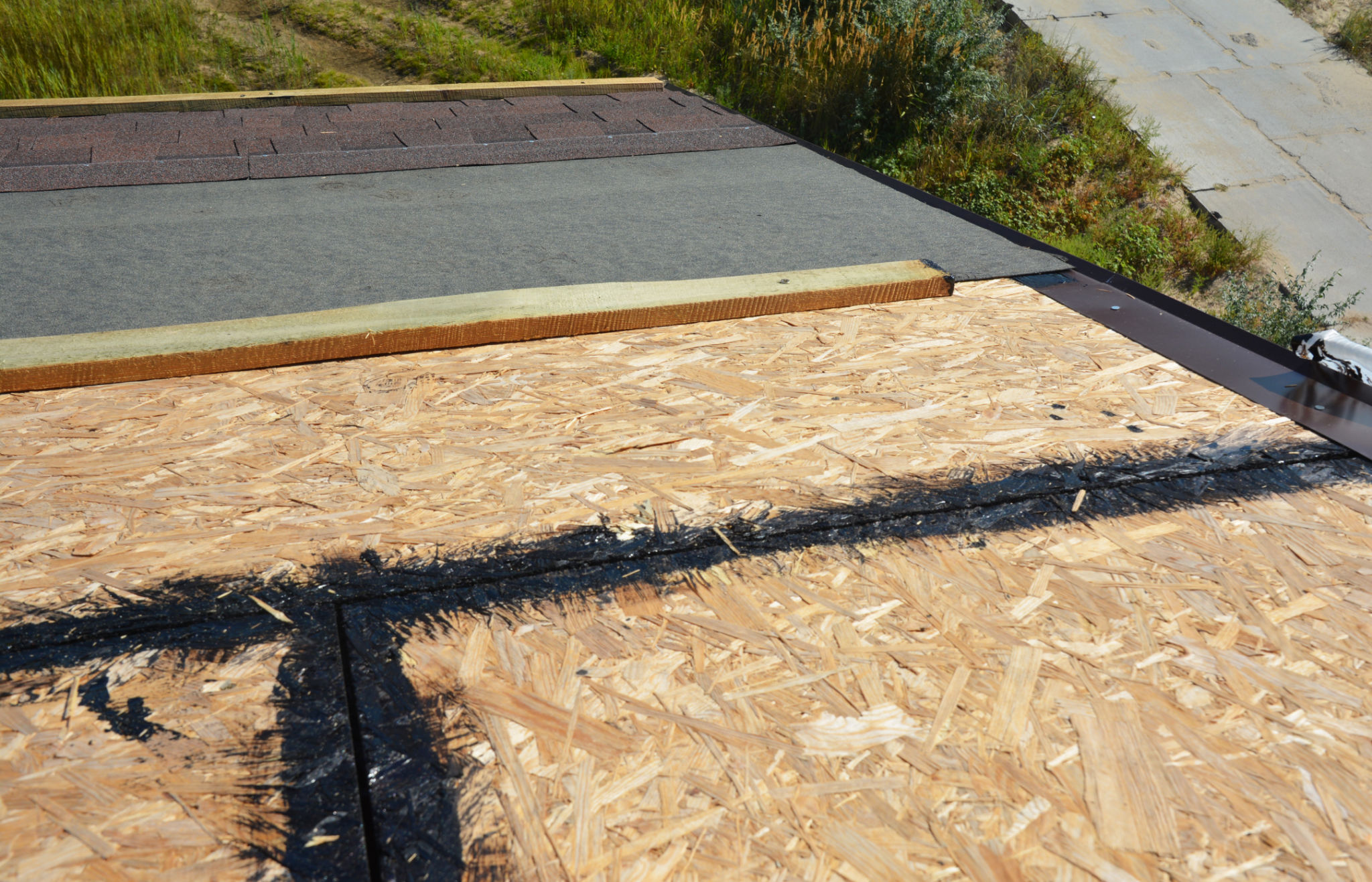 Installing asphalt shingles on the roof. A close-up of asphalt shingles installation layers: waterproofing OSB sheathing with tar, or hot asphalt, underlayment, and eave protection. Installing asphalt shingles on the roof. A close-up of asphalt shingles installation layers: waterproofing OSB sheathing with tar, or hot asphalt, underlayment, and eave protection.
