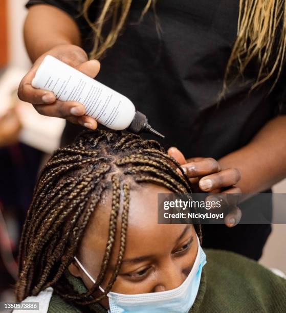 woman in beauty salon getting her braided hair moisturised - hairdressers black woman stockfoto's en -beelden