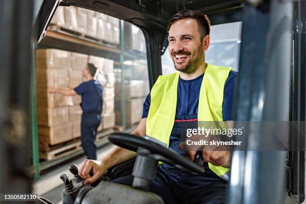 happy manual worker driving forklift in distribution warehouse. - ware house worker forklift stock pictures, royalty-free photos & images