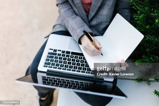 business woman taking notes in a notebook while working with her laptop outdoors. - journalist stock-fotos und bilder