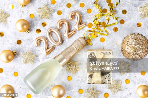 happy new year 2022 greeting card. champagne bottle, gift box, confetti, brass wire stars and ribbon, all on golden color, over gray background. christmas and new year concept. - bottle champagne from above stock pictures, royalty-free photos & images