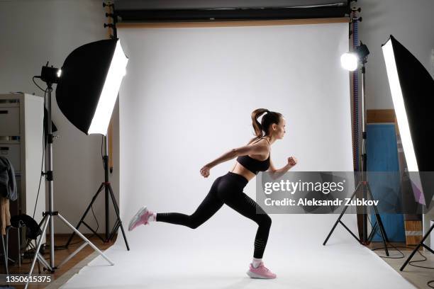 beautiful stylish modern fashionable female runner running in a professional photo and video studio isolated on a white background. simulation of running on camera. the concept of a healthy lifestyle. - fotosession stock-fotos und bilder
