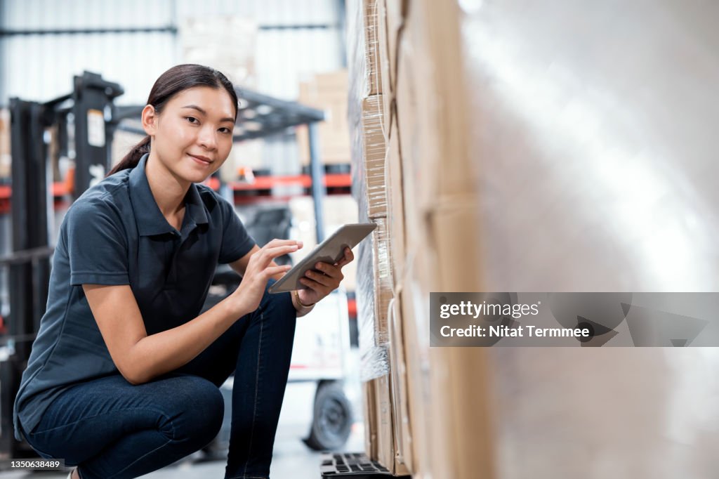 Stock Handling and Inventory Control Process. Side View of Asian Female Warehouse worker working on a digital tablet to record the stock that is actually on the shelf in a distribution warehouse.