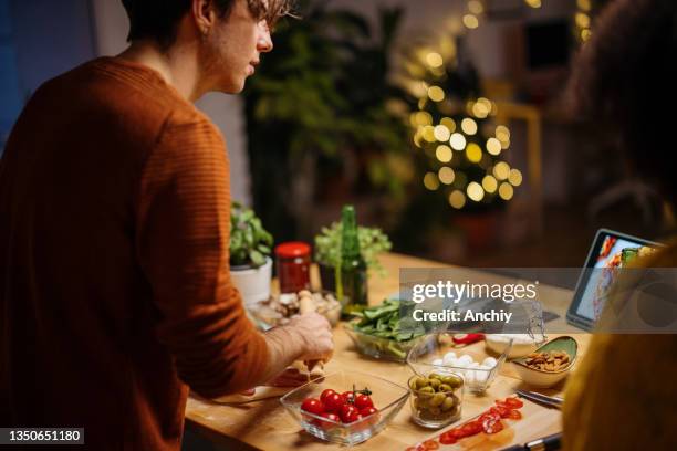 young man looking at digital tablet and talking to his girlfriend while preparing pizza for dinner - cooking event stock pictures, royalty-free photos & images