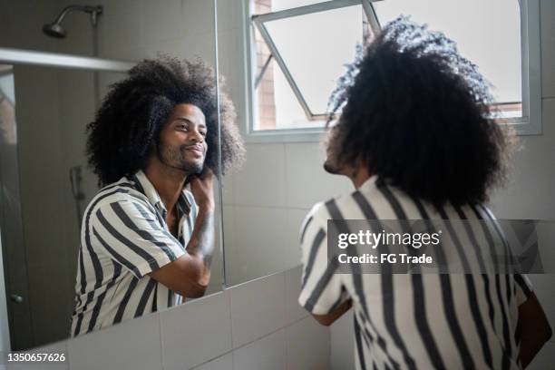 young man admiring himself in the mirror - man hair care stock pictures, royalty-free photos & images