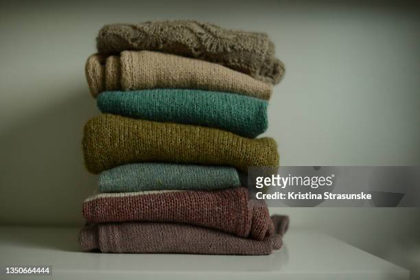 a stack of knitted sweaters in brown and green color tones on a white shelf - vestito marrone foto e immagini stock
