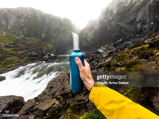 optical illusion refilling reusable insulated water bottle from waterfall in iceland. - ilusión óptica fotografías e imágenes de stock