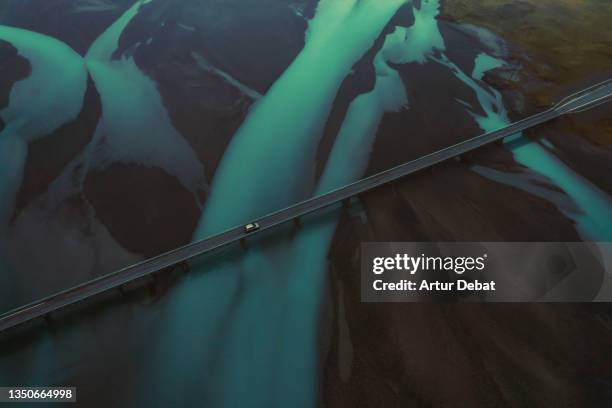 drone view of a car crossing a bridge in iceland with blue steams of glacier water. - great river road stock pictures, royalty-free photos & images