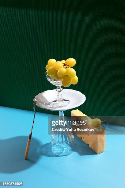 green grapes , cheese, plate, fork and wine glasses on the puren-blue background - still life fotografías e imágenes de stock