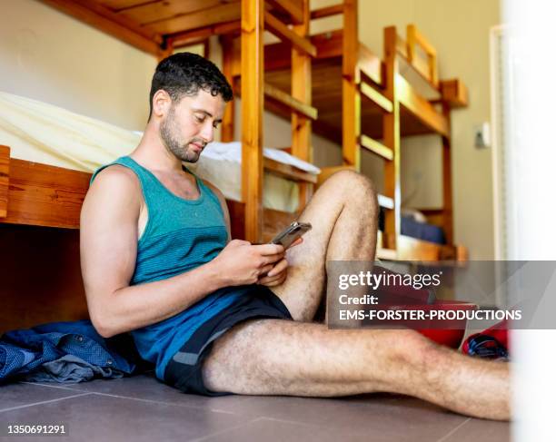 young adult student sitting in a room eith bunk beds and using mobile phone - litera fotografías e imágenes de stock